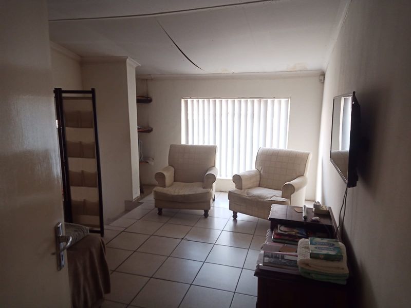 A living room featuring tiled flooring and vertical blinds, currently showing signs of ceiling damage and wear.