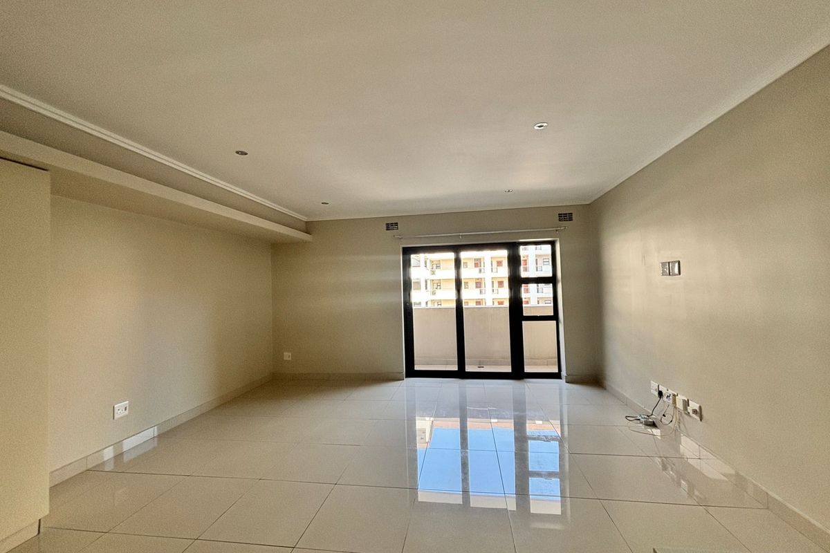 A spacious, empty living area featuring neutral tiled flooring, recessed downlighting, and a large sliding glass door providing access to the exterior.