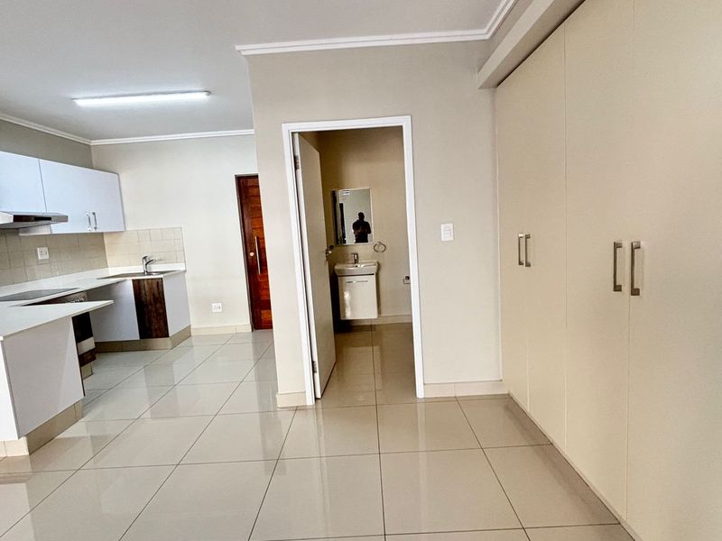 Open plan living area featuring a modern kitchen with built-in cabinetry, tiled flooring, and ample storage space, leading to a separate bathroom.