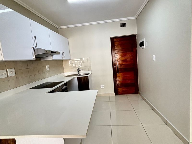 Modern kitchen featuring white cabinetry, stone countertops, integrated hob, extractor fan, and tiled flooring, presenting a clean and functional space.