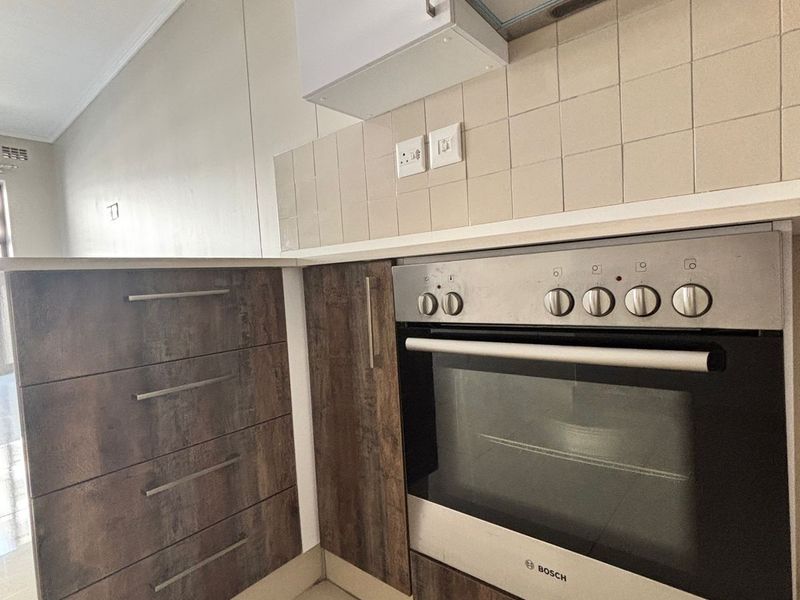A compact kitchen area featuring modern wood-look cabinetry, a built-in Bosch oven, stainless steel extractor fan, and neutral tiled backsplash.