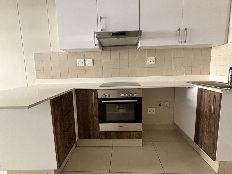 A clean, modern kitchen featuring two-tone cabinetry, stone countertops, built-in oven and hob, and neutral tiled flooring.