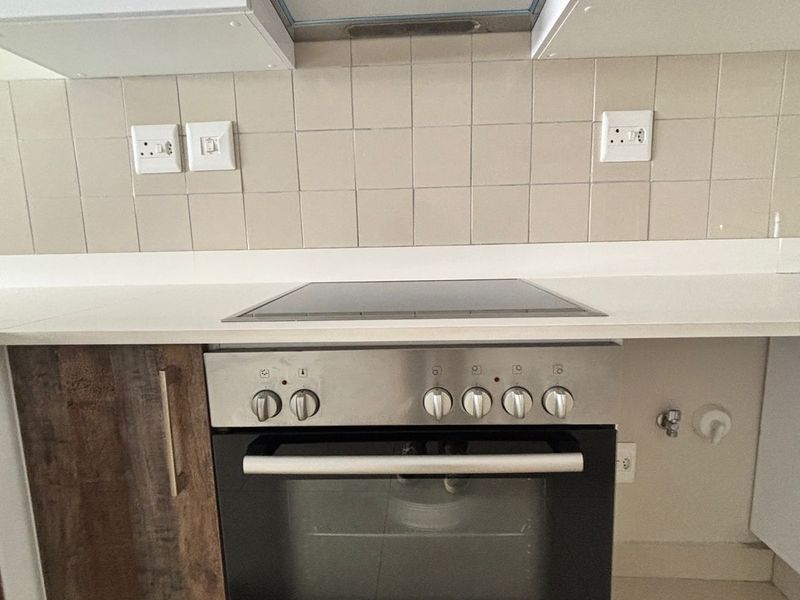 A clean kitchen area featuring a built-in Bosch oven, electric hob, stainless steel extractor fan, and modern cabinetry with a tiled backsplash.