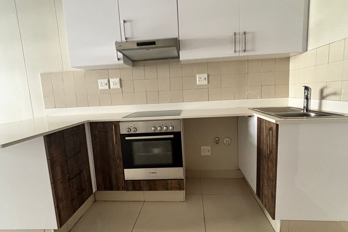A clean, modern kitchen featuring white and wood-tone cabinetry, a built-in oven with hob, extractor fan, and neutral tiled flooring.