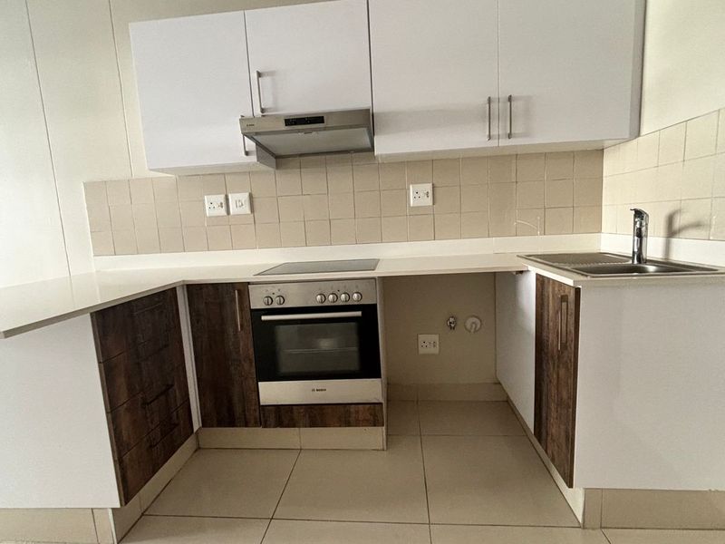 A clean, modern kitchen featuring white and wood-tone cabinetry, a built-in oven with hob, extractor fan, and neutral tiled flooring.