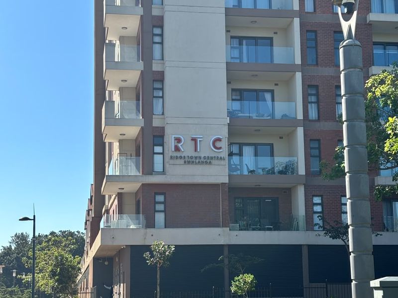 A clear exterior view of the Ridge Town Central apartment building, showcasing its modern brick facade, glass balconies, and well-maintained surrounding grounds.