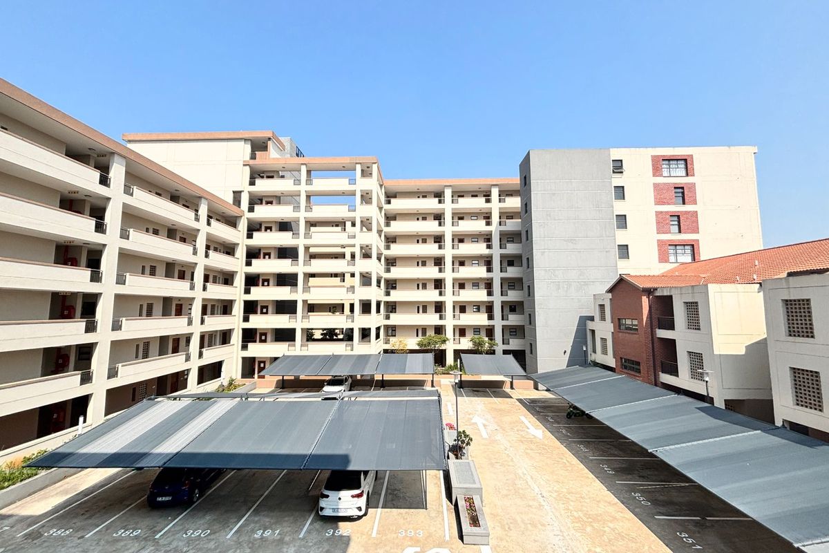 View of a multi-story apartment complex featuring paved parking areas with covered bays and multiple residential balconies.