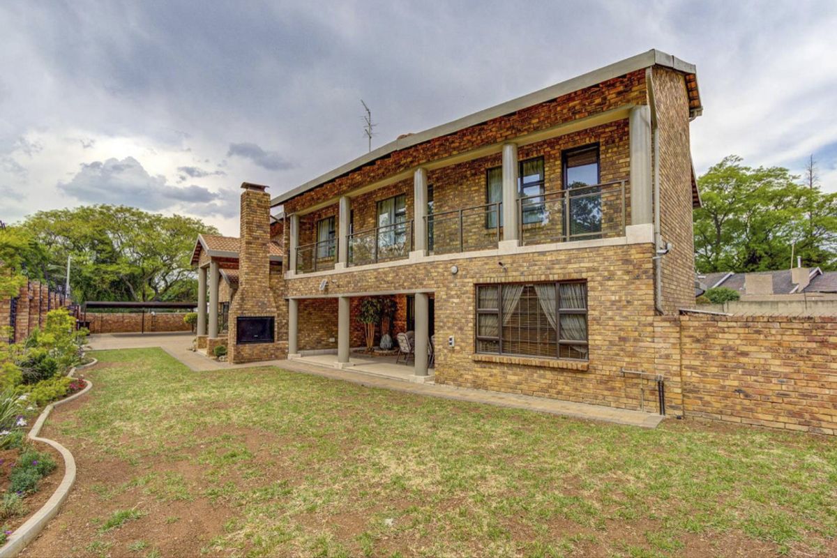 Rear view of a double-story face brick house featuring a covered patio with an outdoor fireplace and an upper-level balcony with glass balustrades.
