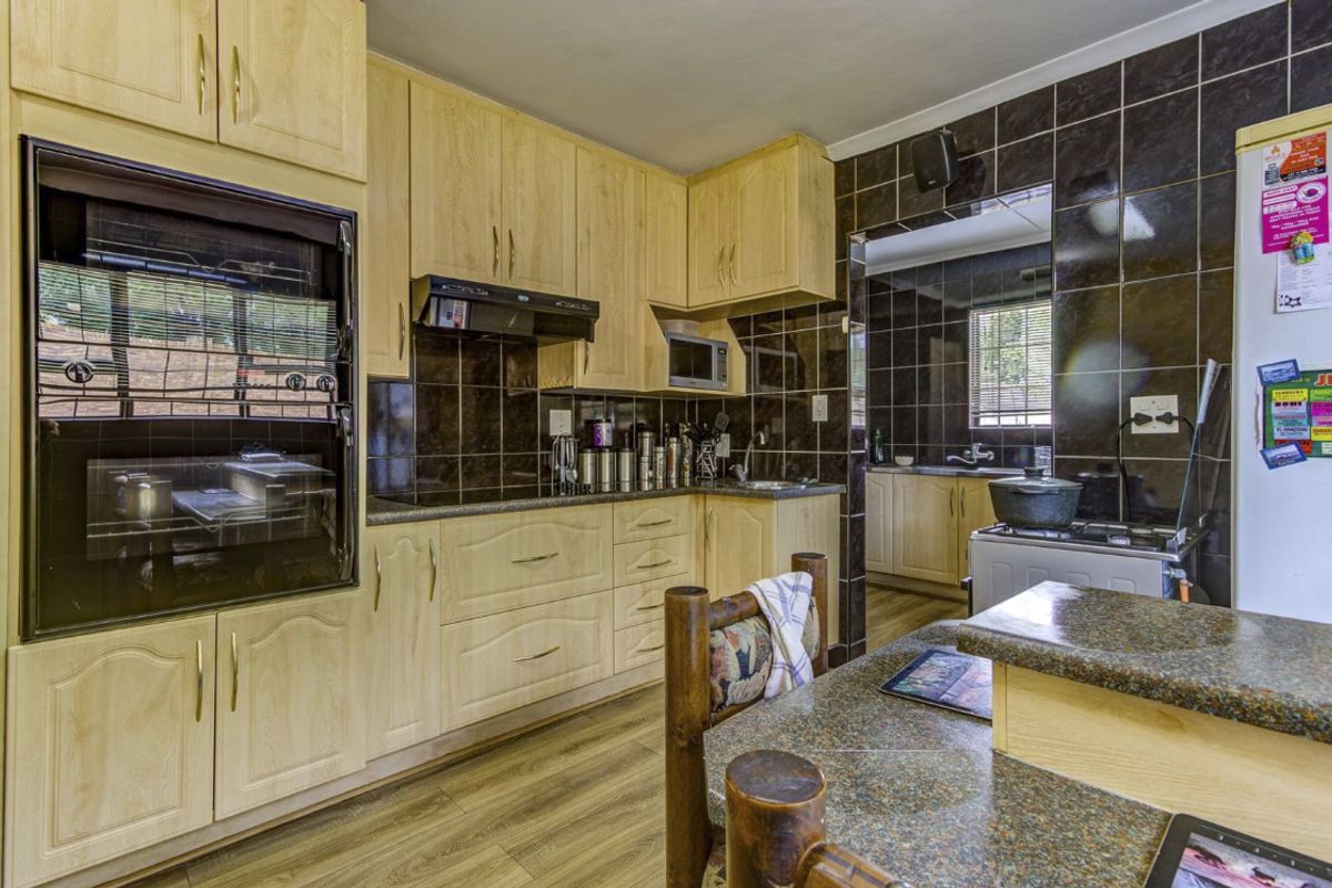 A functional kitchen featuring light wood cabinetry, dark tiled splashbacks, built-in oven, and a stone-look countertop with an adjacent scullery area.
