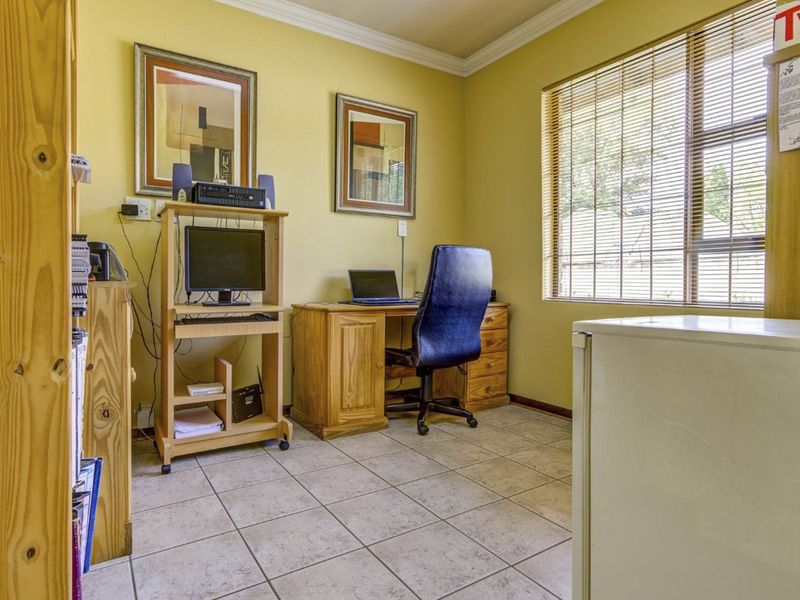 A functional home office space featuring tiled flooring, crown molding, and a large window with fitted blinds, providing natural light for a workspace.