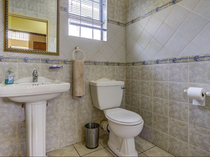 A functional bathroom featuring a pedestal sink, toilet, and neutral ceramic wall and floor tiling with decorative border accents.