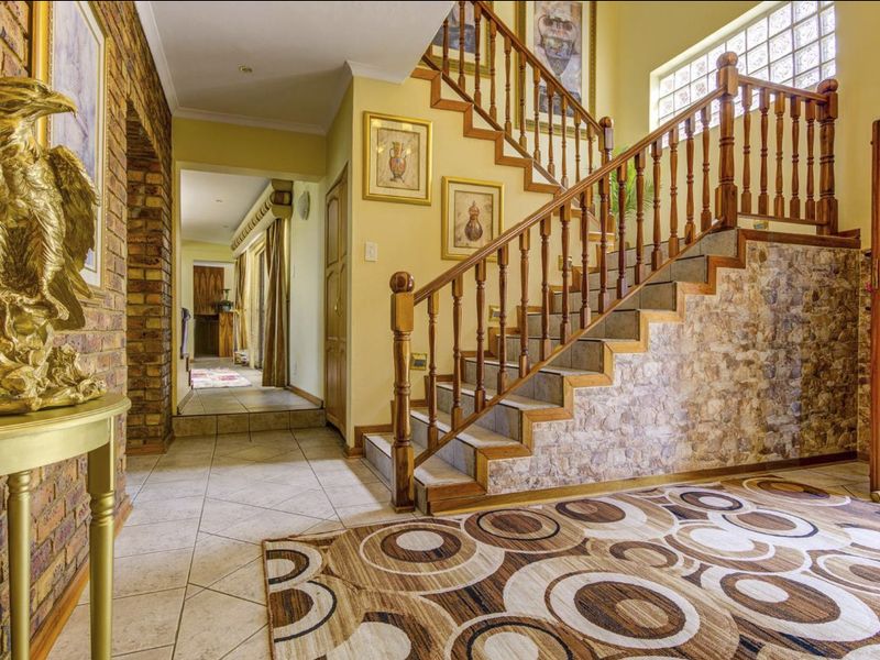 Spacious entrance hall featuring a timber staircase, exposed brickwork, stone-clad accents, and ceramic tile flooring leading to a connecting hallway.