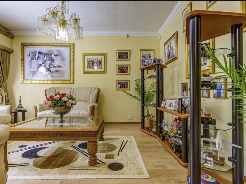 A well-maintained living room featuring crown molding, laminate flooring, and a decorative crystal chandelier, offering a traditional and cozy atmosphere.