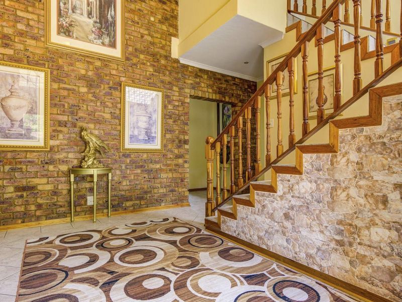 Entrance foyer featuring a striking exposed brick wall, stone-clad staircase base, and traditional wooden balustrade with tiled flooring.