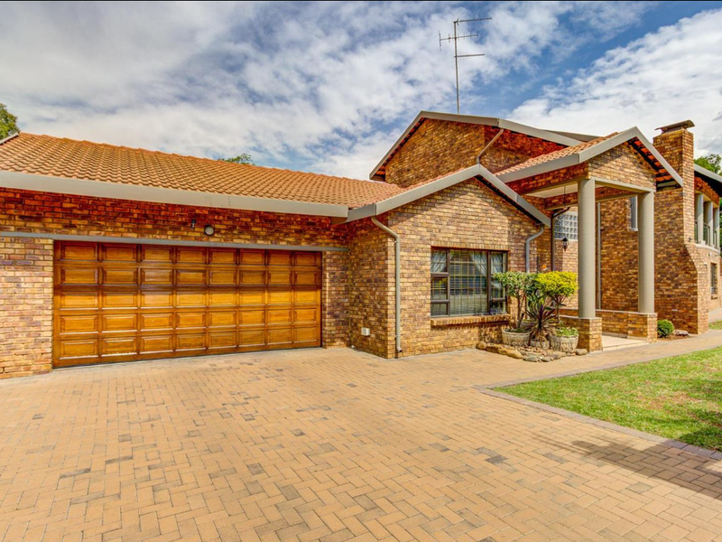 Front elevation of a face-brick house featuring a paved driveway, double garage, and a covered entrance with architectural columns.