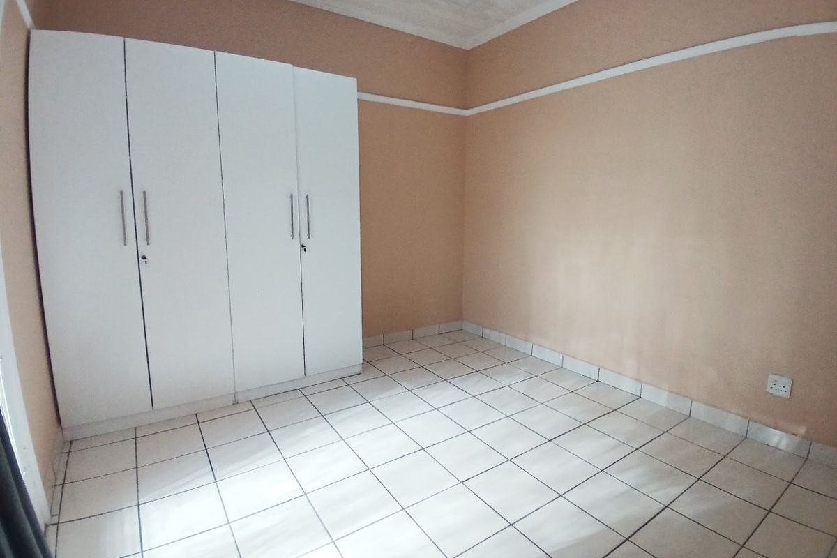 An empty bedroom featuring white tiled flooring, a built-in wardrobe, and neutral wall tones, offering a blank canvas for personalization.