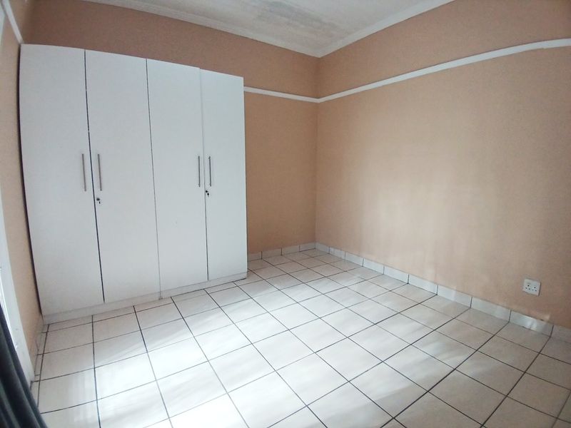 An empty bedroom featuring white tiled flooring, a built-in wardrobe, and neutral wall tones, offering a blank canvas for personalization.
