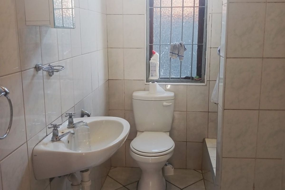 A compact bathroom featuring tiled walls and flooring, a wall-mounted basin, and a standard toilet, with security bars installed on the window.