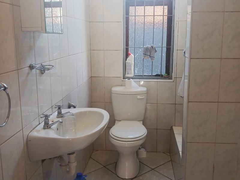 A compact bathroom featuring tiled walls and flooring, a wall-mounted basin, and a standard toilet, with security bars installed on the window.