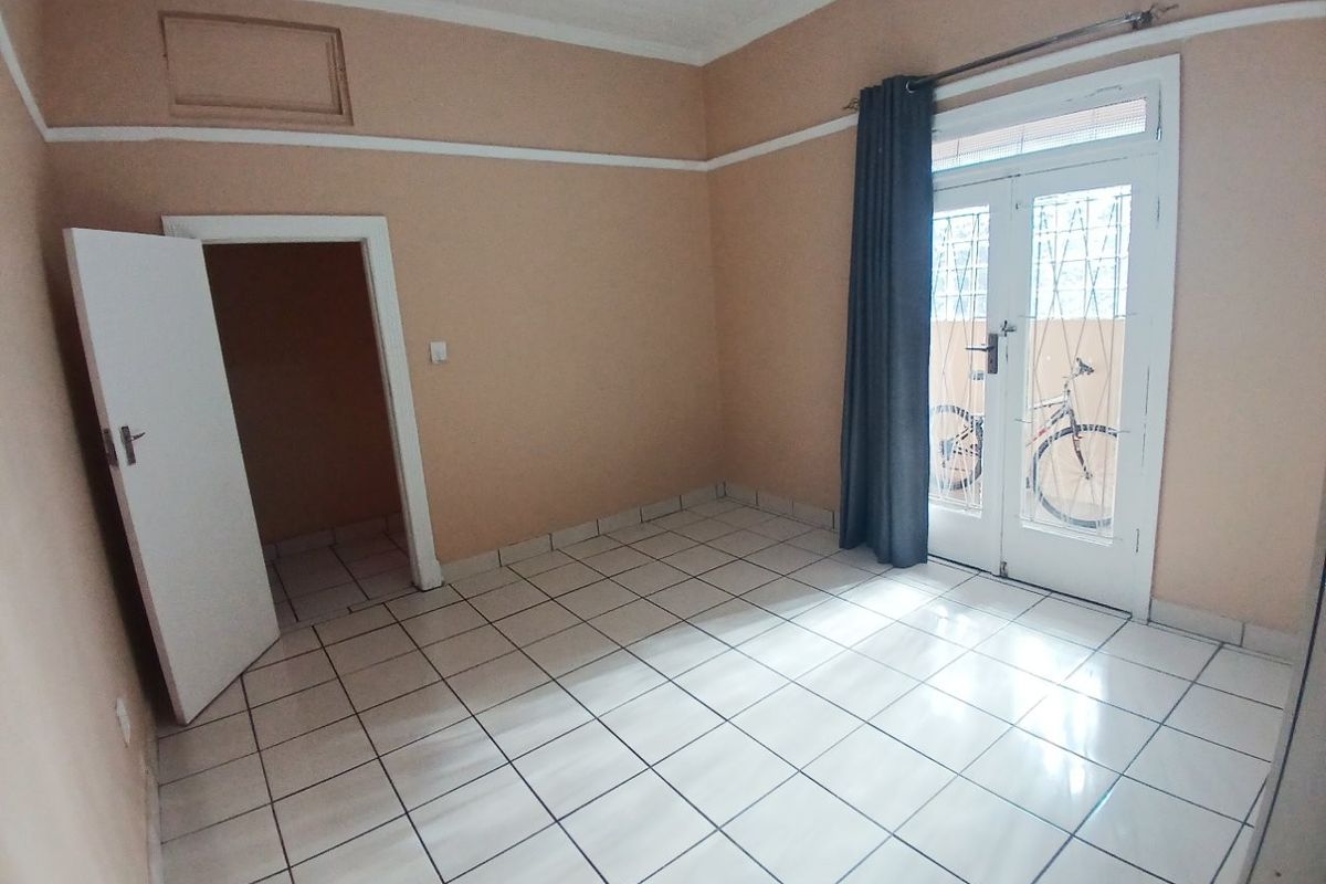 An empty bedroom featuring tiled flooring, neutral walls, and a double glass door providing access to the exterior.
