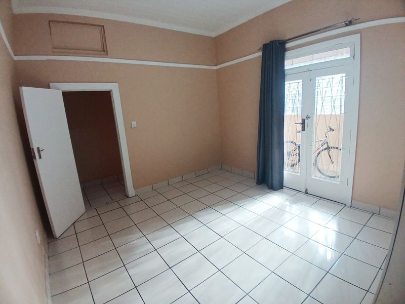 An empty bedroom featuring tiled flooring, neutral walls, and a double glass door providing access to the exterior.