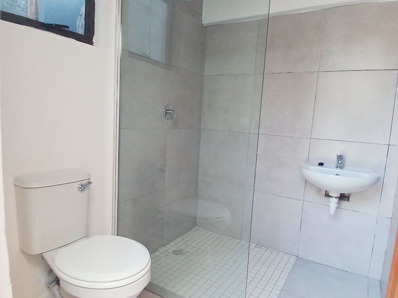 A functional bathroom featuring a glass-enclosed shower, wall-mounted basin, and toilet, with neutral wall and floor tiling.