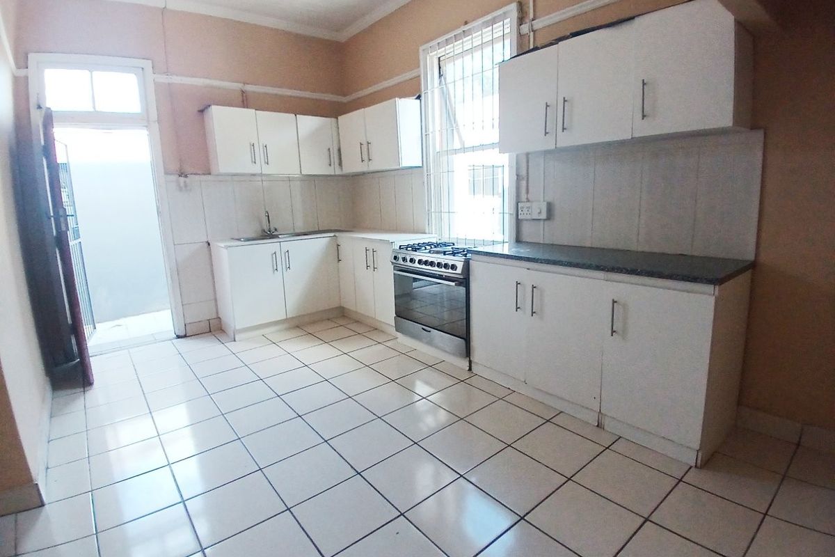A functional kitchen featuring white cabinetry, tiled flooring, a stainless steel stove, and a tiled backsplash, offering a clean canvas for potential updates.