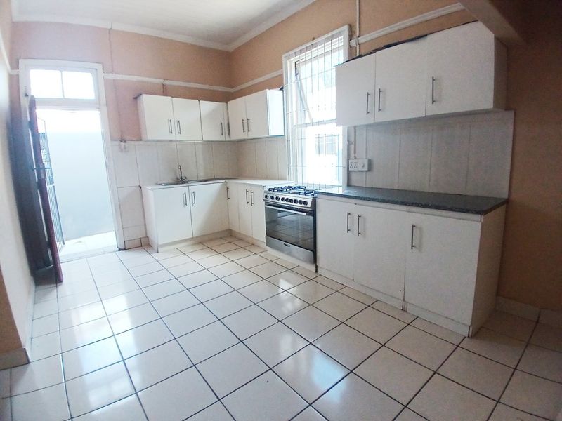 A functional kitchen featuring white cabinetry, tiled flooring, a stainless steel stove, and a tiled backsplash, offering a clean canvas for potential updates.