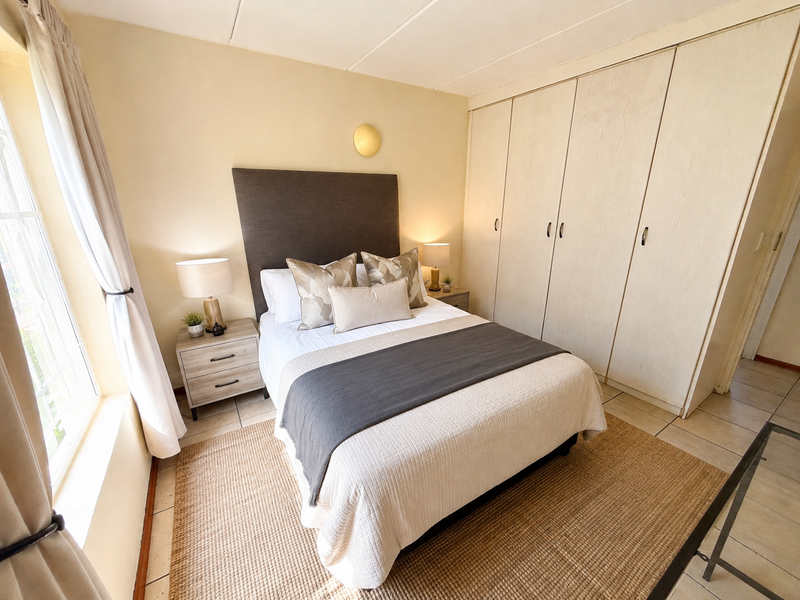 A well-lit bedroom featuring built-in cupboards, tiled flooring, and a window with security bars, offering a functional and comfortable living space.