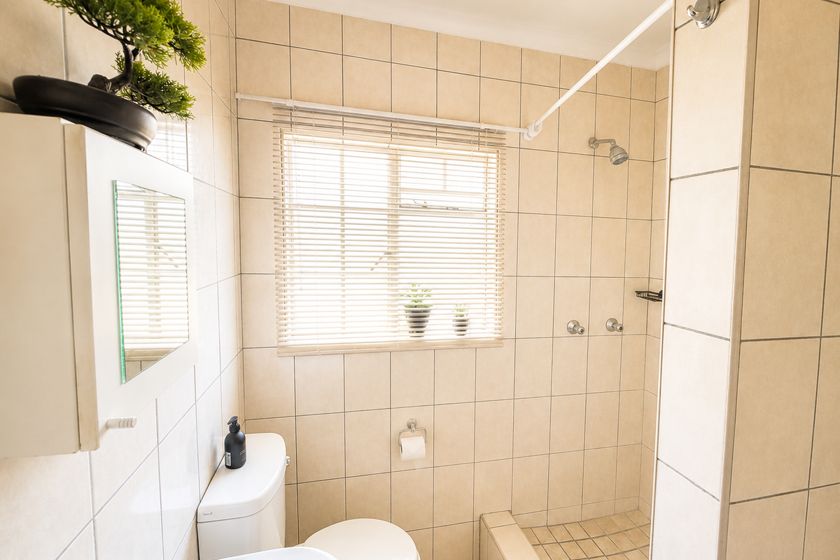 A functional bathroom featuring neutral wall and floor tiles, a built-in shower area, a toilet, and a wall-mounted medicine cabinet.