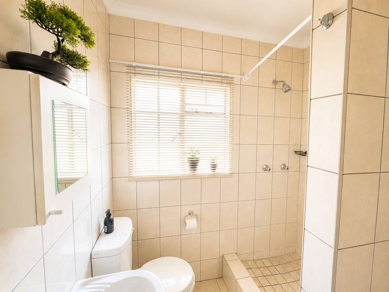 A functional bathroom featuring neutral wall and floor tiles, a built-in shower area, a toilet, and a wall-mounted medicine cabinet.