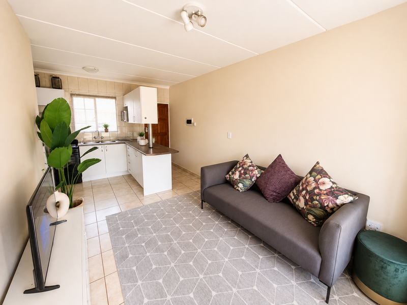 Open-plan living area featuring a functional kitchen with white cabinetry, laminate countertops, and tiled flooring throughout the combined space.