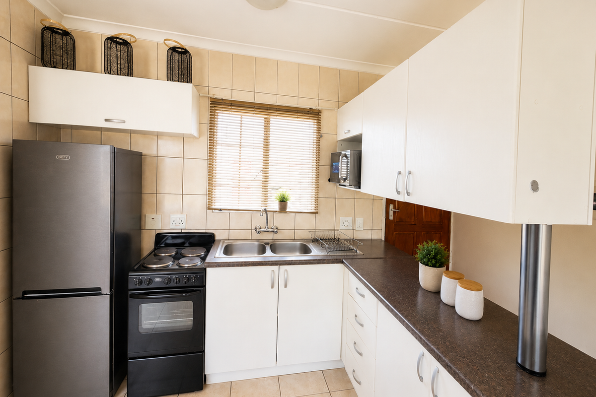 A functional kitchen featuring white cabinetry, dark laminate countertops, a double basin sink, and a freestanding stove with tiled backsplash and flooring.