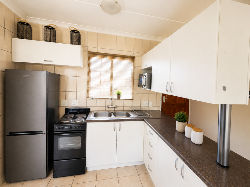 A functional kitchen featuring white cabinetry, dark laminate countertops, a double basin sink, and a freestanding stove with tiled backsplash and flooring.