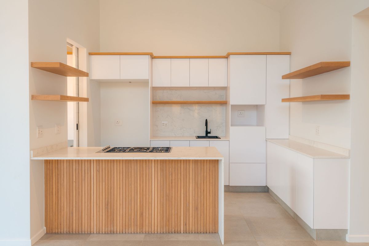 Modern kitchen featuring white cabinetry, timber slat island, stone countertops, floating shelves, and integrated gas hob in a bright, open-plan space.