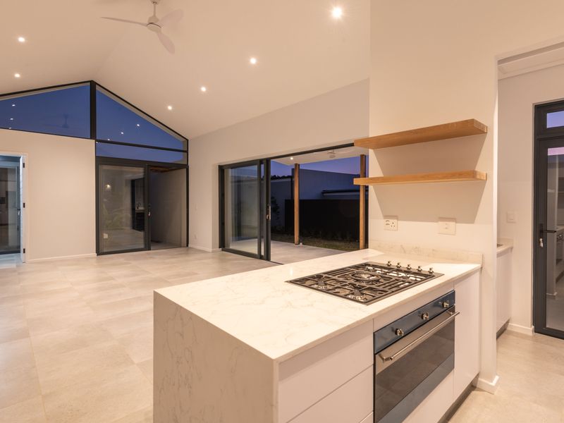 Modern open-plan living area featuring a sleek kitchen island with gas cooktop, stone countertops, and seamless indoor-outdoor flow through large sliding glass doors.