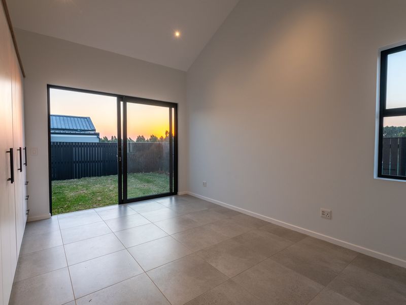 A bright, modern bedroom featuring vaulted ceilings, tiled flooring, built-in cabinetry, and a sliding glass door providing direct access to the rear garden.