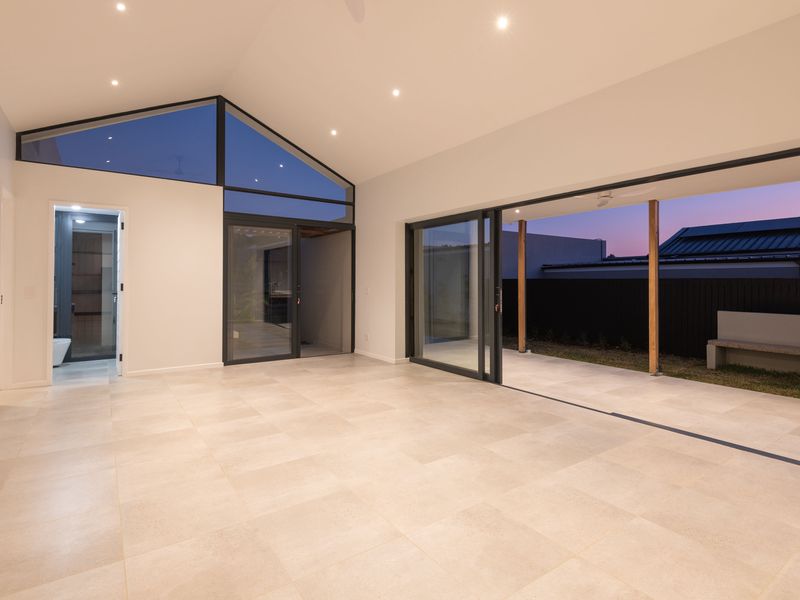 Spacious, modern living area featuring a vaulted ceiling, large format floor tiles, and seamless indoor-outdoor flow through expansive sliding glass doors.