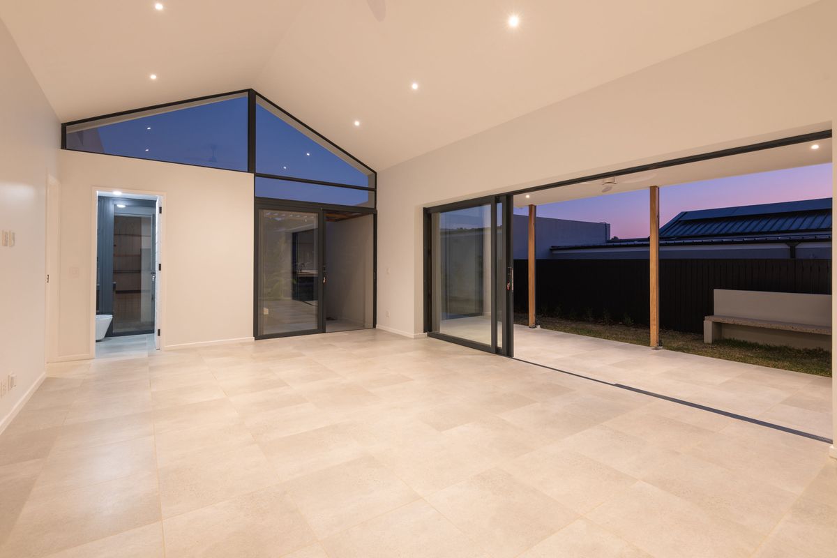 Spacious, modern living area featuring a vaulted ceiling, large format floor tiles, and seamless indoor-outdoor flow through expansive sliding glass doors.