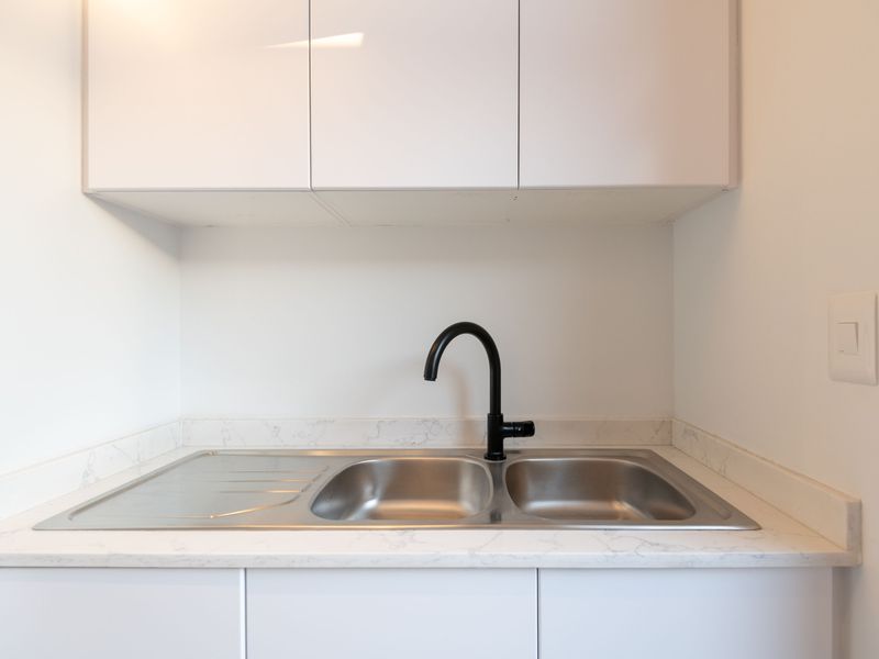 A clean and modern scullery or utility area featuring white cabinetry, a stone-look countertop, and a contemporary black gooseneck faucet with a double sink.