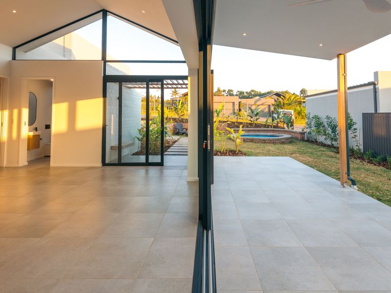 Modern open-plan living area with vaulted ceilings and seamless indoor-outdoor flow to a covered patio, garden, and raised pool area.
