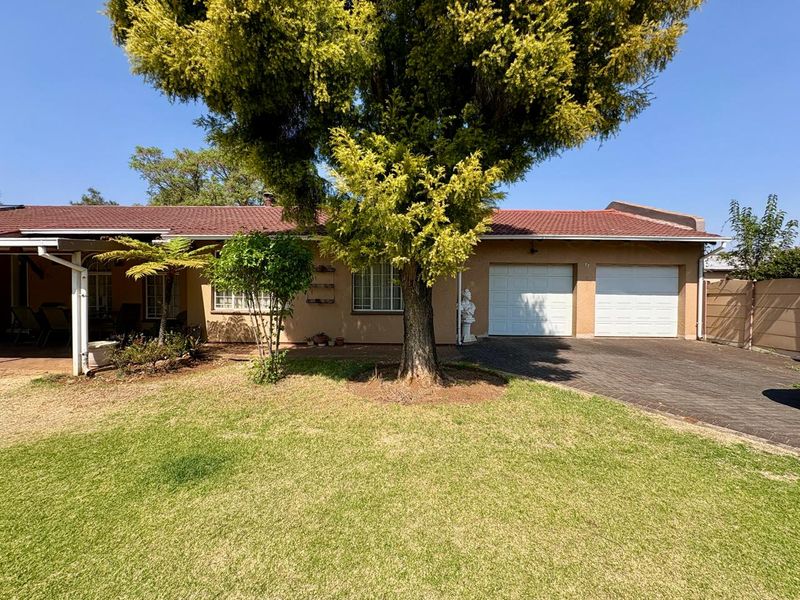 Front view of a single-story house featuring a double garage, paved driveway, covered patio area, and a well-maintained front lawn.