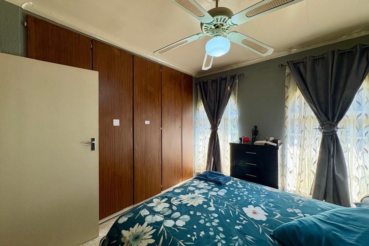 A bedroom featuring built-in wooden cupboards, a ceiling fan, and carpeted flooring, offering a functional and comfortable living space.