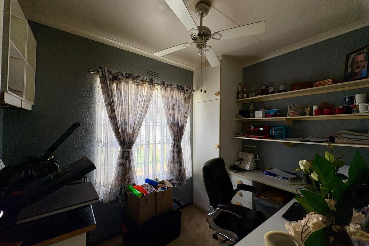 A functional bedroom or home office space featuring built-in shelving, a desk, and a ceiling fan, offering practical storage and workspace solutions.