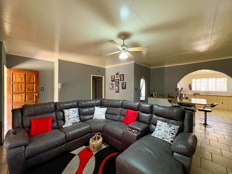 Open plan living area featuring tiled floors, a ceiling fan, and an arched transition into a functional kitchen space with built-in cabinetry.