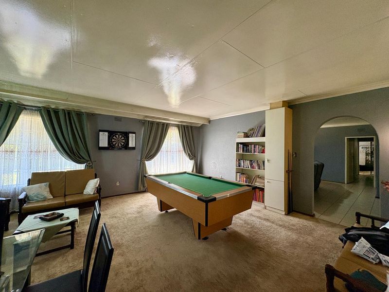Spacious living area featuring a built-in shelving unit, arched doorway, and carpeted flooring, offering a versatile space for relaxation or entertainment.