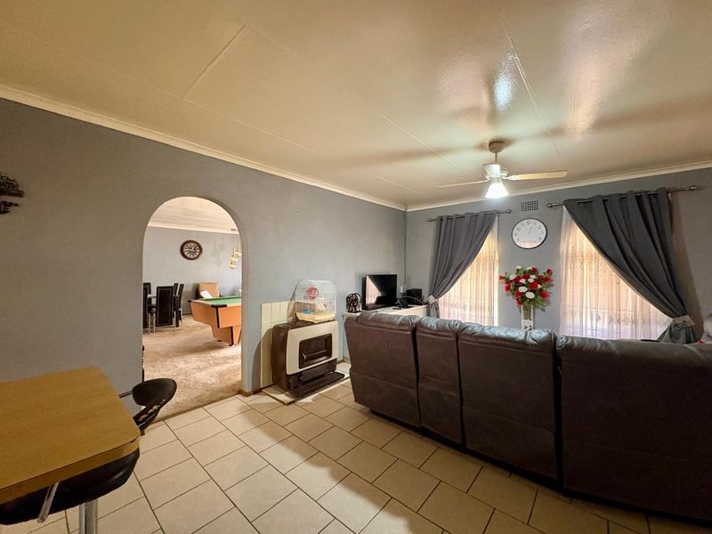 Spacious living room featuring tiled flooring, a ceiling fan, and a built-in gas heater, with an arched entryway leading to an adjacent room.