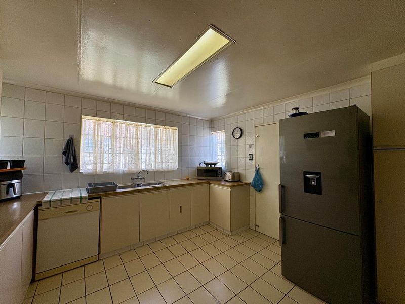 A functional kitchen featuring tiled flooring, tiled splashbacks, laminate countertops, and a double basin sink, offering a dated aesthetic ready for modernization.