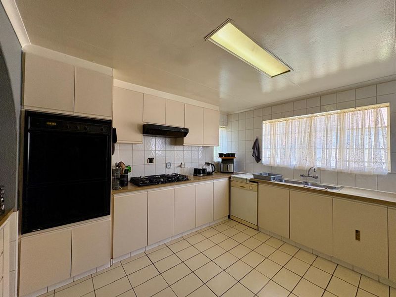 A functional kitchen featuring built-in oven, gas hob, extractor fan, double sink, and tiled finishes, offering a classic layout ready for modern updates.