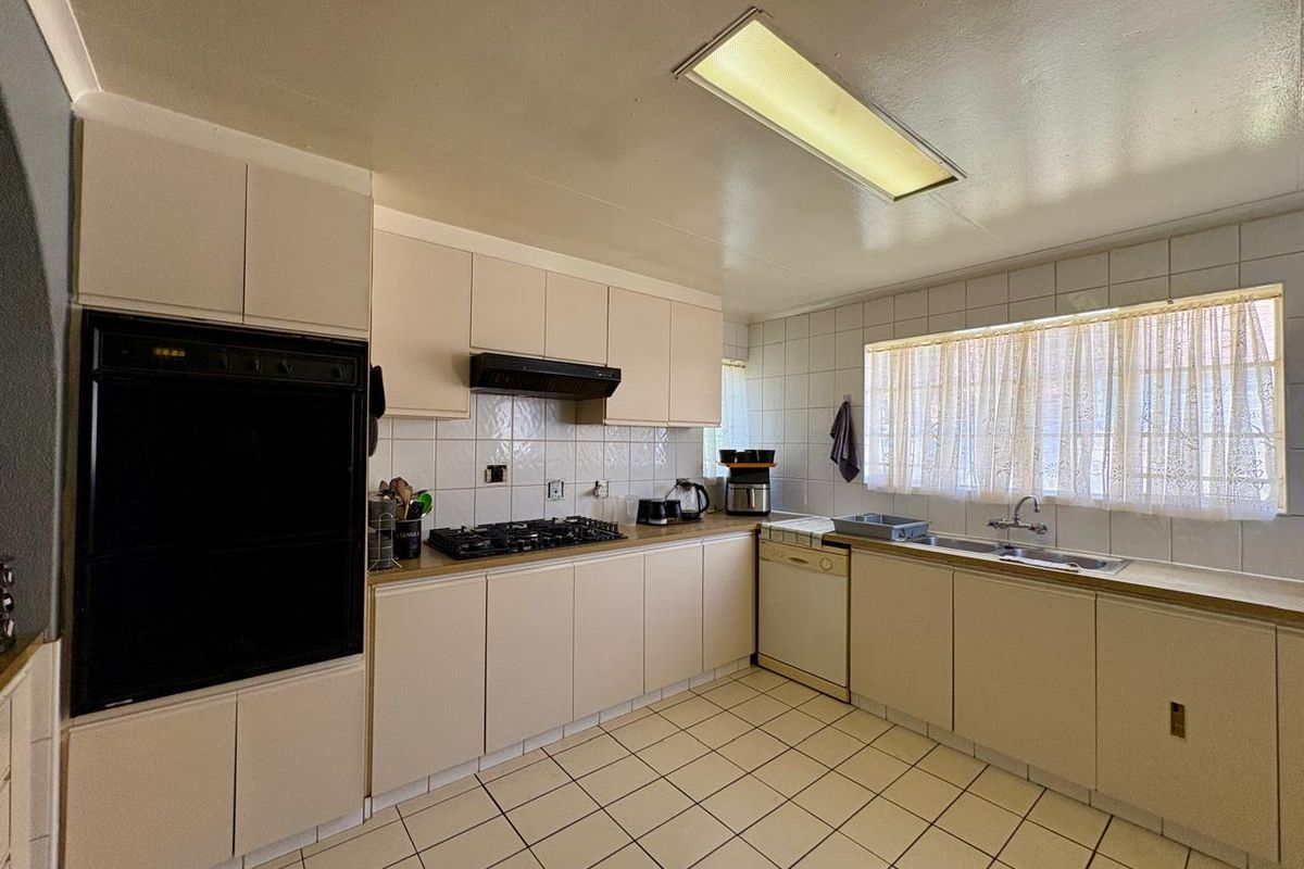 A functional kitchen featuring built-in oven, gas hob, extractor fan, double sink, and tiled finishes, offering a classic layout ready for modern updates.